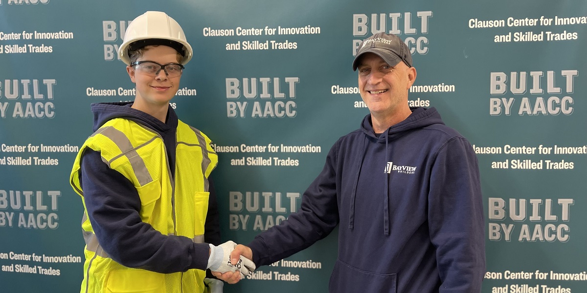 Trevor Churchill in a vest, gloves and hard hat shakes hands with Rich Lang.