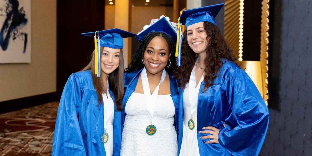 Three AACC students wearing graduation regalia and smiling.