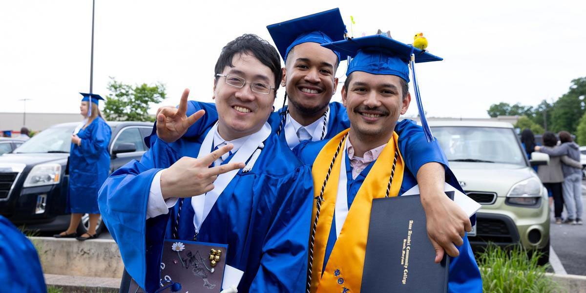 Three AACC students wearing graduation regalia and smiling.