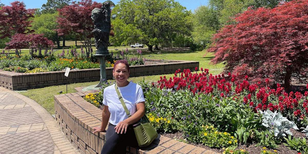 April Copes sitting on a brick wall with flowers blooming in a garden behind her.