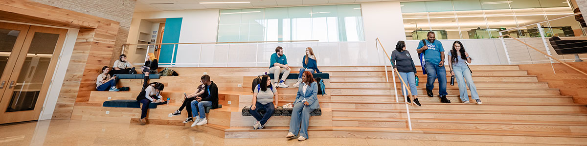 Students sitting on stairs talking. Another group of students walking down the stairs.